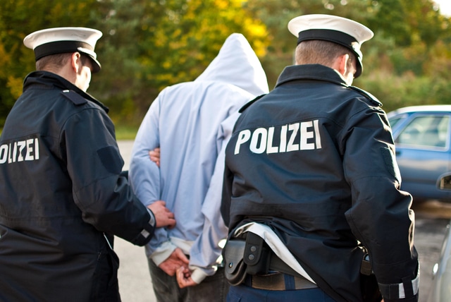 Polizisten führen einen Festgenommenen ab – Ermittlungen bei Kapitaldelikten