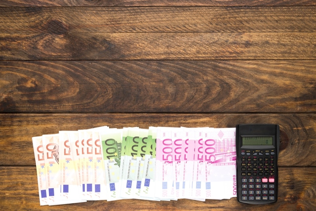 Euro-Banknoten und Taschenrechner auf Holztisch – offene Forderungen berechnen
