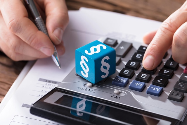 Taschenrechner mit Paragraphen-Würfel und Stift – Schmerzensgeld berechnen